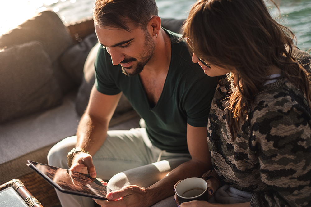 Couple smiling and watching tablet screen by the river